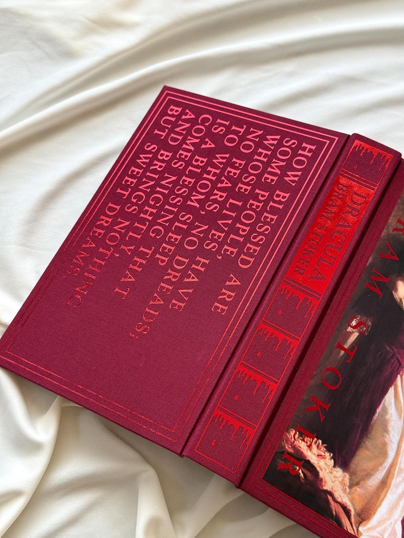 May include: A red hardcover book with the title "Dracula" by Bram Stoker. The book cover features a portrait of a woman in a white dress with a red background.