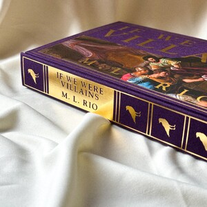 May include: A purple hardback book with gold lettering that reads "If We Were Villains" by M.L. Rio. The book cover features a painting of a group of people in a dramatic scene.