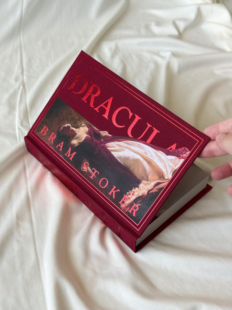May include: A red hardcover book titled "Dracula" by Bram Stoker. The cover features a painting of a woman lying down in a white dress.