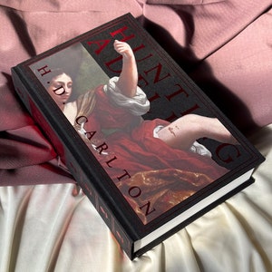 Puede incluir: Un libro de tapa dura negro con el t&iacute;tulo "A Hunting Adieu" en letras rojas. La portada del libro presenta una pintura de una mujer con un vestido rojo y un brazo levantado.