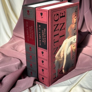 Puede incluir: Dos libros de tapa dura con cubiertas rojas y negras. El libro de la derecha tiene el t&iacute;tulo "HAUNTING ADELINE" y el autor "H.D. CARLTON". El libro de la izquierda tiene el t&iacute;tulo "HUNTING ADELINE" y el autor "H.D. CARLTON".