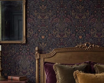 Op de afbeelding: Een slaapkamer met donker bloemenbehang, een goudkleurige spiegel en een houten nachtkastje met een koperen kandelaar. Een bed met een gouden hoofdeinde is opgemaakt met een dieppaars fluwelen dekbed en bijpassende fluwelen kussens.
