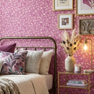 Pode incluir: Quarto com papel de parede floral em tons de rosa e creme. Cama com almofadas decorativas, um cobertor de pele sintética e uma estrutura de metal dourado. Obras de arte e uma mesa de cabeceira com livros e uma lâmpada.