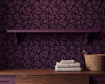 Op de afbeelding: Een donkerpaarse muur met een herhalend acanthusbladpatroon, een houten plank en een donkerhouten kast. Een stapel gevouwen lichtgekleurde handdoeken ligt op het kastoppervlak naast een gevlochten mand, onder een hangende koperen lamp.