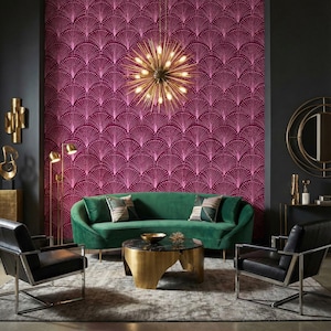 Pode incluir: Um sofá curvo de veludo verde com duas almofadas estampadas, uma mesa de centro redonda de mármore preto com base dourada e duas poltronas de couro preto com estruturas prateadas, diante de um papel de parede magenta com padrão de leque.