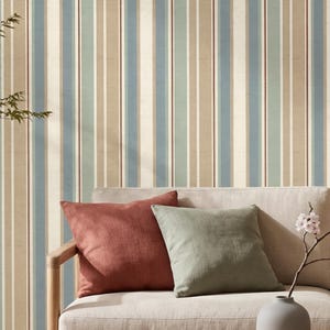 May include: A light-coloured sofa with a rust-coloured cushion and a sage green cushion. A light wood coffee table holds a grey vase with a small branch. The wall behind features vertical stripes in shades of beige, blue, green, and thin brown lines.