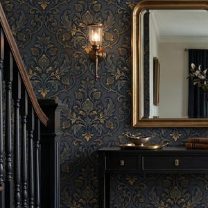 May include: Dark blue wallpaper with a gold and bronze damask pattern featuring ornate floral motifs. A black console table sits below a gold-framed mirror and a wall-mounted light fixture with a glass shade, next to a dark wooden staircase.