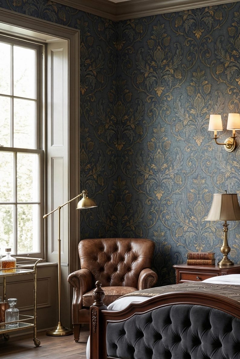 May include: A luxurious bedroom with dark blue wallpaper featuring a gold floral pattern. A tufted brown leather armchair sits near a window. A brass floor lamp and a bedside table with a lamp and books complete the elegant decor.