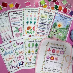 Peut inclure: Une collection de guides de points de broderie et un cerceau de broderie rose avec un panneau de tissu blanc montrant différents types de points de fleurs volumétriques. Les guides sont imprimés sur du papier blanc avec de l'encre noire et présentent différents points de broderie, notamment le point de contour, le point de couverture, le point de marguerite paresseuse, le point de chaînette et les nœuds français. Les guides sont disposés sur une surface rose avec du fil à broder coloré.