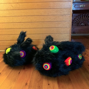 May include: A pair of black faux fur slippers featuring multiple protruding, spherical accents in bright neon colors including green, yellow, orange, and purple, each with a concentric circular pattern on the surface of the spheres.