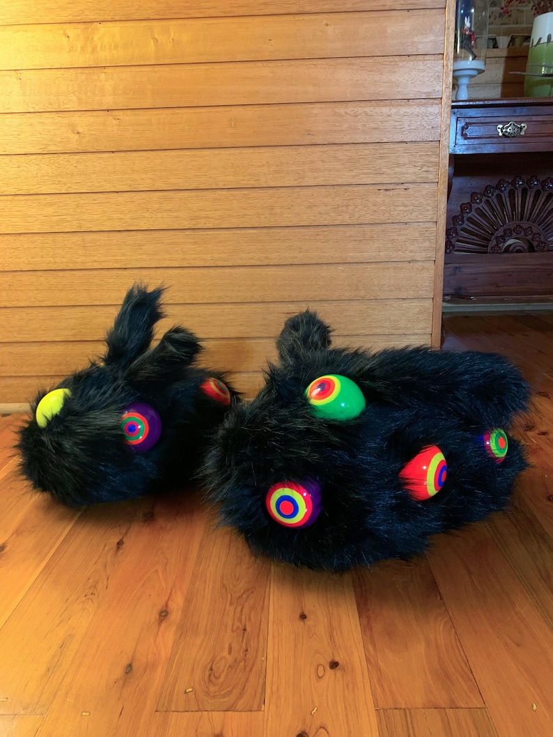 May include: A pair of black faux fur slippers featuring multiple protruding, spherical accents in bright neon colours including green, yellow, orange, and purple, each with a concentric circular pattern on the surface of the spheres.