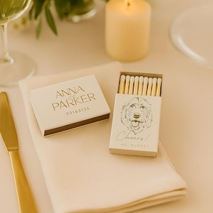 May include: A wedding table setting with a lit candle, floral arrangement, and a gold knife. Two matchboxes are visible, one with the text "Anna & Parker" and the other with a dog illustration and the word "Cheers!"