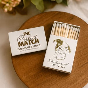 May include: Two white matchboxes on a wooden surface. One box reads "THE Perfect MATCH" with names and a date. The other box, open, features a dog illustration and the text "Drinks or me! LOVE, HALIFAX". The matches are visible inside.