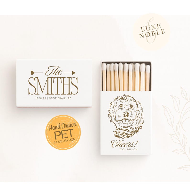 White wedding matchboxes featuring a hand drawn dog illustration with the word “Cheers!” and the text “XO, Dillon” in elegant gold lettering. The outer sleeve reads “The Smiths” with an arrow motif and a date and location printed below. Personalized pet inspired wedding favors for couples.