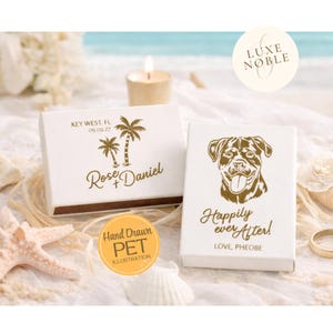 May include: Two white boxes with gold text and illustrations. One box has palm trees and the text "Key West, FL 09.09.27" and "Rose + Daniel". The other box has a dog illustration and the text "Happily ever After! Love, Pheobe".
