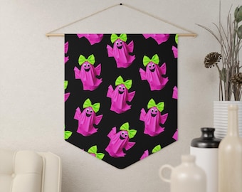 May include: A black wall banner featuring a repeating pattern of bright pink ghosts. Each ghost has two large black eyes, a wide smiling mouth, and a vibrant lime green bow attached to the top of its head. The banner is suspended by a thin string.