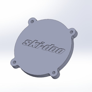 May include: A gray, circular part with the word "Ski-doo" embossed on the surface. The part has four evenly spaced, circular protrusions around the edge. The object appears to be made of a solid material.