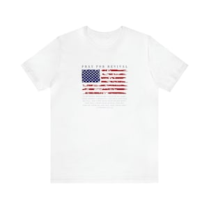 May include: White t-shirt with a distressed American flag design and the text "Pray for Revival" and a Bible verse from 2 Chronicles 7:14.