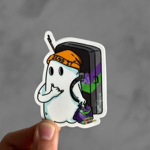 May include: A white ghost wearing an orange hat with the text "SEND IT" on it. The ghost is holding a black and green climbing wall with a purple and green climbing hold.