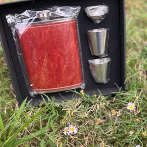 May include: A red leather-covered flask with a silver lid and three silver shot glasses in a black box.