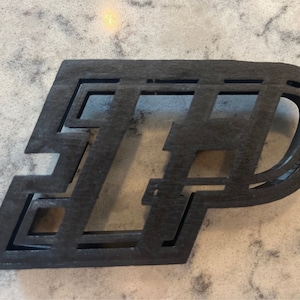 May include: A black wooden cutout of the letters "IP" in a layered design.