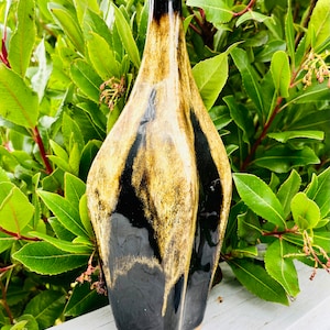 Puede incluir: Un jarrón de cerámica negro y dorado con una forma abstracta única. El jarrón tiene un acabado brillante y es perfecto para exhibir flores u otros artículos decorativos.