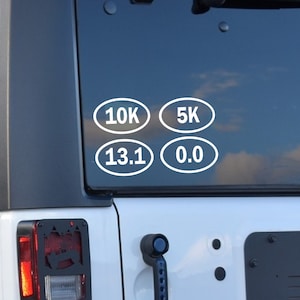 May include: Four white oval stickers on a black car window. The stickers show the distances 10K, 5K, 13.1, and 0.0.