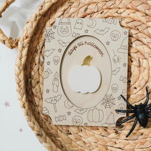 May include: A wooden Halloween countdown plaque with a white pumpkin and gold stem. The plaque is decorated with Halloween-themed doodles and the words "days till halloween". Two black plastic spiders are on the sides.
