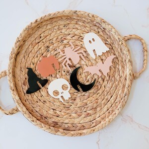 May include: A wicker tray with a variety of Halloween-themed decorations, including a ghost, a bat, a spider, a witch's hat, a skull, and a crescent moon.