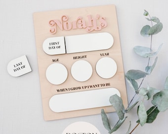 May include: A wooden growth chart with a pink inscription that reads "Norah's". The chart has spaces to record the child's first and last day of life, age, height, year, and a space for the child to write what they want to be when they grow up.