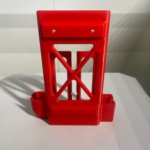 K&ouml;nnte beinhalten: Ein leuchtend rotes, 3D-gedrucktes Objekt mit einem rechteckigen Rahmen und einem offenen, geometrischen Design. Es hat zwei kleine Seitenf&auml;cher und eine zentrale, kreuzf&ouml;rmige St&uuml;tzstruktur. Oben sind zwei L&ouml;cher sichtbar.