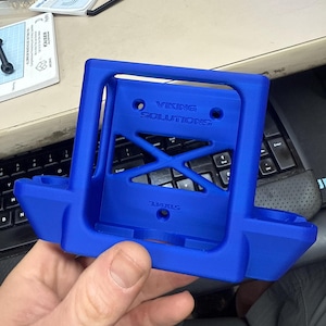 K&ouml;nnte beinhalten: Ein leuchtend blauer, 3D-gedruckter Halter mit dem Text "VIKING SOLUTIONS" und einem X-f&ouml;rmigen Design in der Mitte. Der Halter hat einen rechteckigen Rahmen mit zwei abgerundeten Abschnitten.