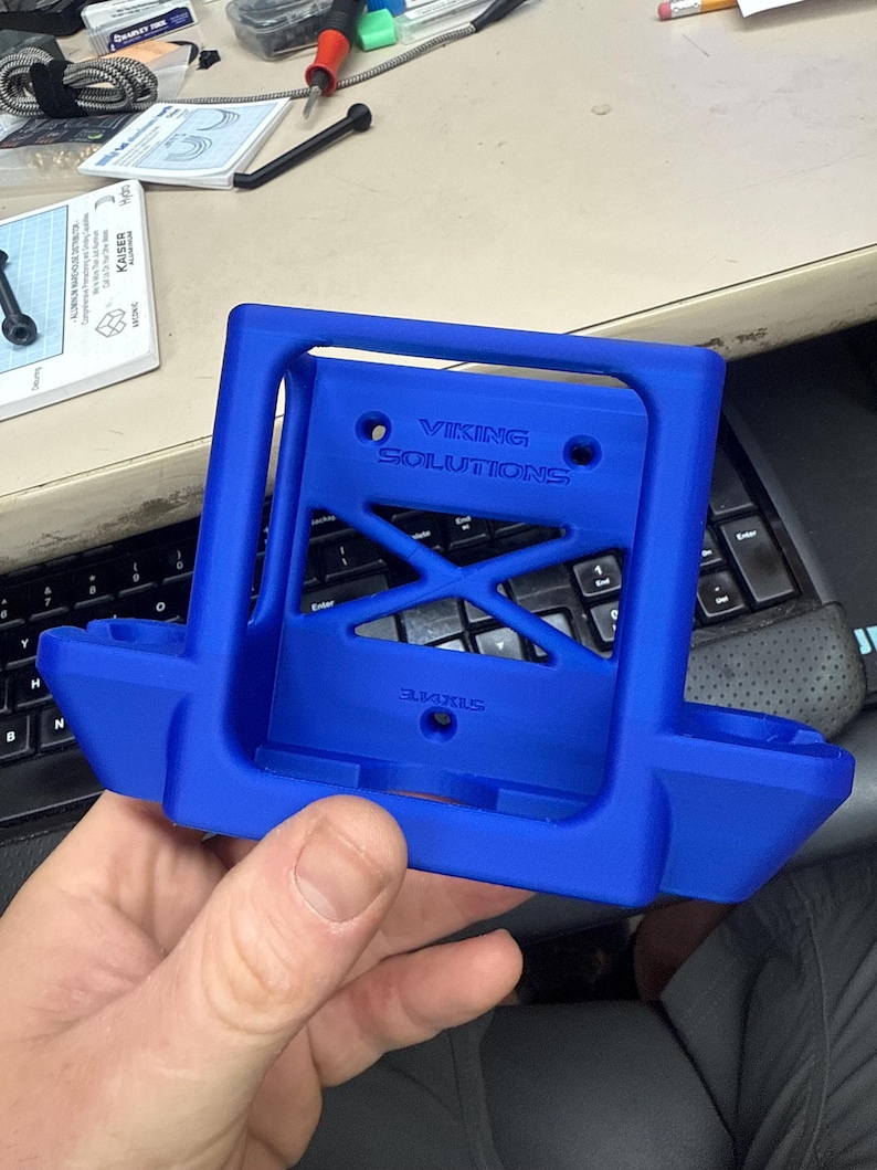 K&ouml;nnte beinhalten: Ein leuchtend blauer, 3D-gedruckter Halter mit dem Text "VIKING SOLUTIONS" und einem X-f&ouml;rmigen Design in der Mitte. Der Halter hat einen rechteckigen Rahmen mit zwei abgerundeten Abschnitten.