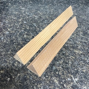 May include: Two wooden triangular pieces, one with a smooth surface and the other with a textured surface. Both pieces are made of light wood.