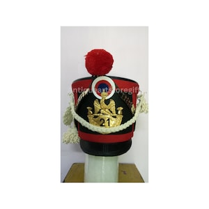 Può includere: Un cappello militare nero e rosso con un emblema di aquila dorata e il numero 21. Il cappello ha un bordo di corda bianca e un pompon rosso in cima.