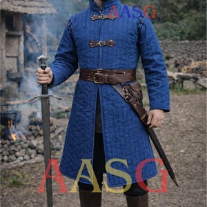 May include: A blue quilted medieval coat with brown leather belt and accents. The coat has a high collar and is fastened with leather straps. A sword is held in one hand. The coat is knee-length and worn with brown boots.