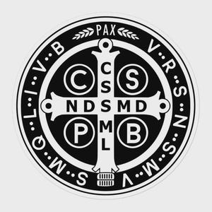 Può includere: Un emblema religioso rotondo in bianco e nero con la parola "PAX" in alto e varie lettere e simboli. L'emblema presenta una croce al centro con le lettere "CSS", "NDSMD" e "PMB".