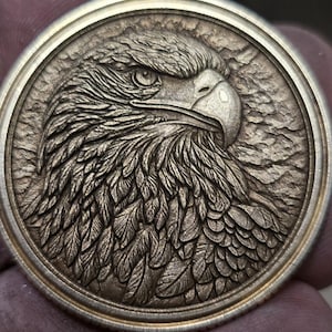以下が含まれることがあります： 鷲の横顔が浮き彫りされた、詳細な円形のコイン。 鷲の目は見え、羽は精巧に彫られています。 コインは金属的な外観で、おそらく銀または金で、テクスチャード加工された背景があります。