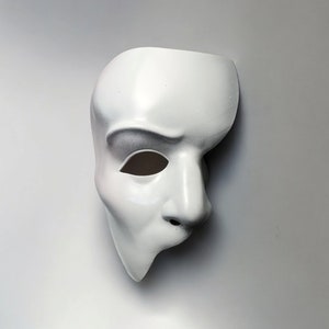 Könnte beinhalten: Eine weiße Plastik-Maskenballmaske mit einem Augenloch und einer modellierten Nase und einem Mund.