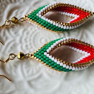 May include: A pair of dangle earrings with a green, white, and red beaded design. The beads are arranged in a twisted pattern and the earrings have gold hooks.