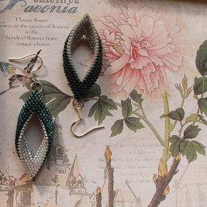 May include: A pair of green and white beaded earrings with a diamond-shaped opening in the center. The earrings are hanging from gold hooks.