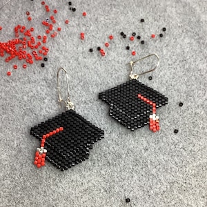 May include: A pair of black and red beaded earrings shaped like graduation caps. The earrings are hanging from silver hooks.
