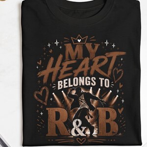 May include: A black short-sleeved t-shirt featuring a graphic print with the text "MY HEART BELONGS TO R&B" in brown and white, accompanied by an illustration of a person dancing under stage lights, surrounded by small heart and star icons.