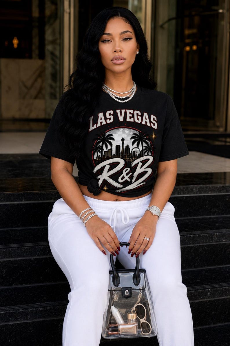 May include: A black short-sleeve t-shirt featuring a graphic print of the Las Vegas skyline with palm trees and the text Las Vegas R&B. The shirt is paired with white drawstring sweatpants and a clear plastic handbag containing small personal items.