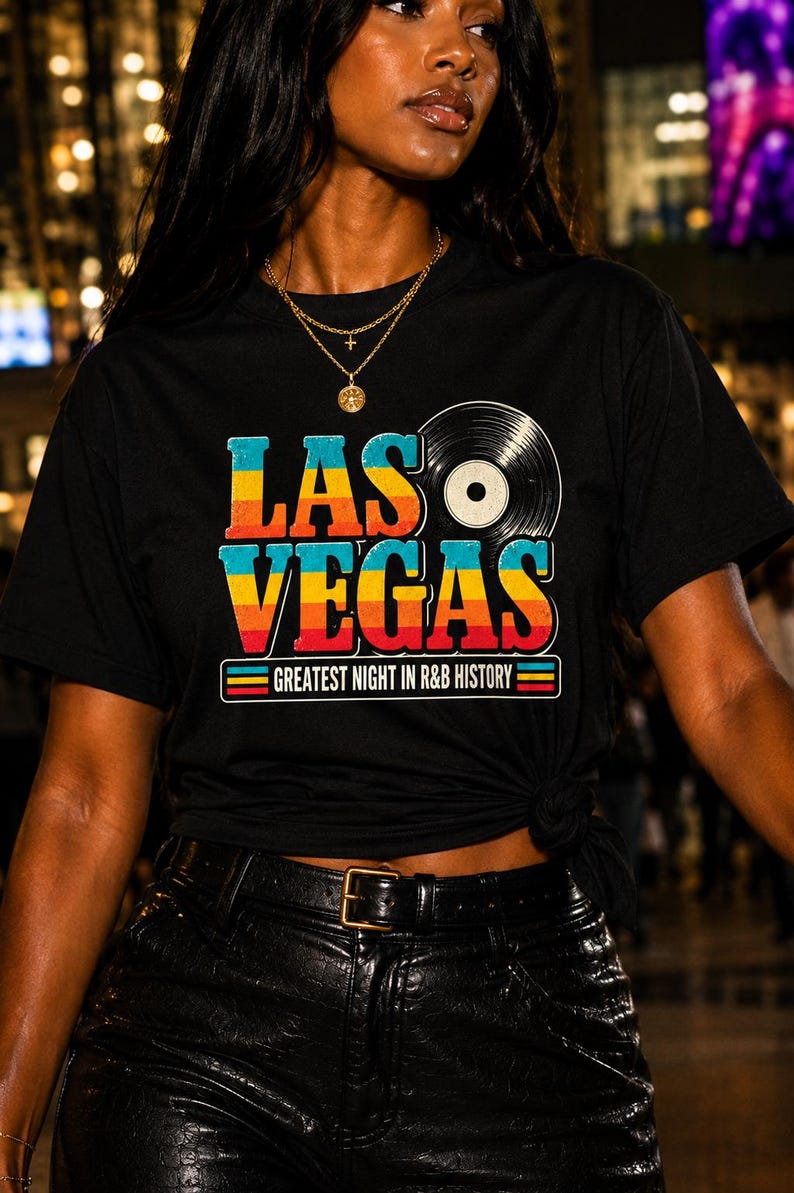 May include: A black short-sleeve t-shirt featuring a graphic print with the text LAS VEGAS in a multi-colored gradient font, a vinyl record icon, and the text GREATEST NIGHT IN R&B HISTORY enclosed in a rectangular border with horizontal stripes.
