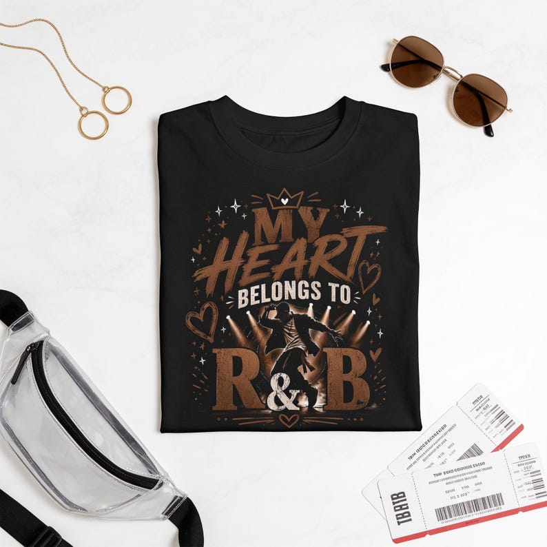 May include: A black short-sleeved t-shirt featuring a graphic print with the text "MY HEART BELONGS TO R&B" in brown and white, accompanied by an illustration of a person dancing under stage lights, surrounded by small heart and star icons.