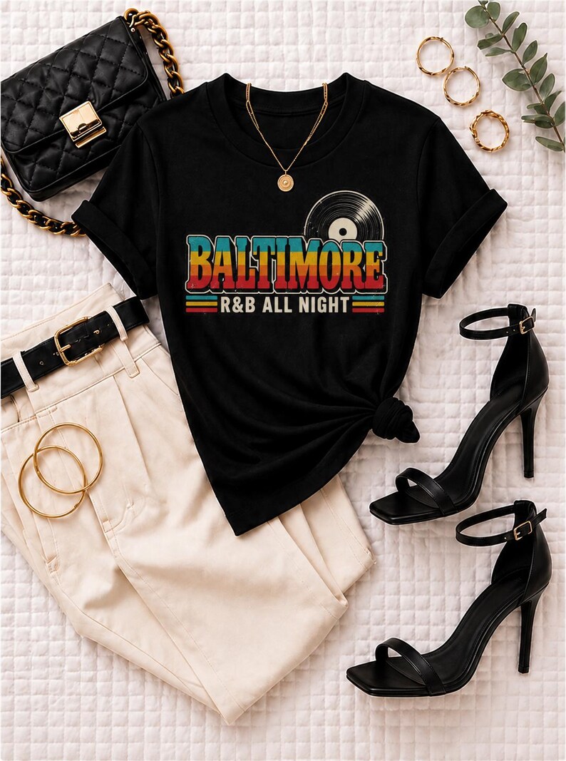 Puede incluir: Una camiseta negra de manga corta con un gr&aacute;fico de un disco de vinilo y el texto BALTIMORE R&B ALL NIGHT en letras de colores retro, combinada con pantalones color crema, un cintur&oacute;n negro, un bolso acolchado negro y sandalias de tac&oacute;n.