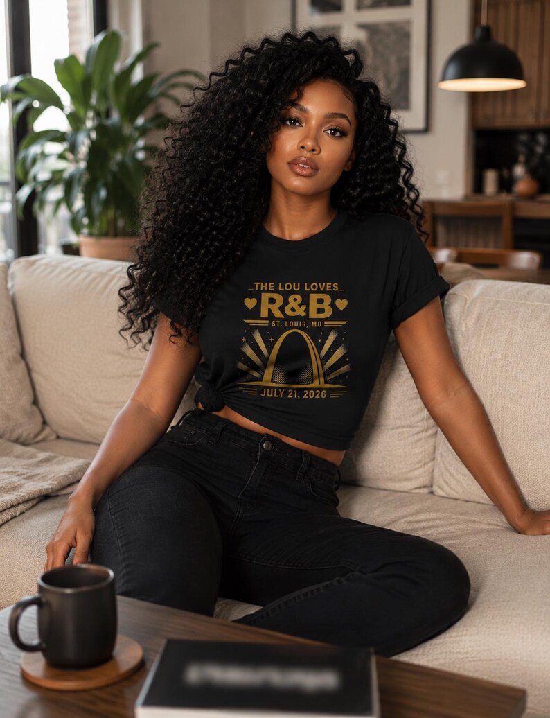 May include: A black short-sleeved t-shirt featuring a gold graphic print that reads THE LOU LOVES R&B, ST. LOUIS, MO, and JULY 21, 2026, centered above an illustration of the Gateway Arch with radiating sunburst lines and small heart icons.
