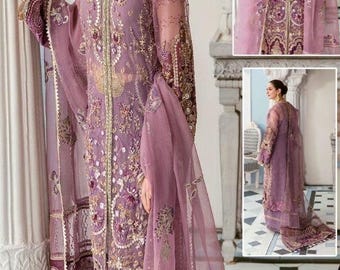 May include: A lavender-colored formal dress with intricate gold embroidery and embellishments. The dress features a sheer overlay and a matching dupatta. The design includes a V-neckline and long sleeves. The dress is suitable for special occasions.