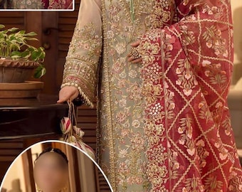 May include: An intricately embroidered, long-sleeved dress in muted green and beige tones, adorned with gold floral patterns. The dress features a matching red shawl with a diamond and floral design. The ensemble is a traditional garment, suitable for special occasions.